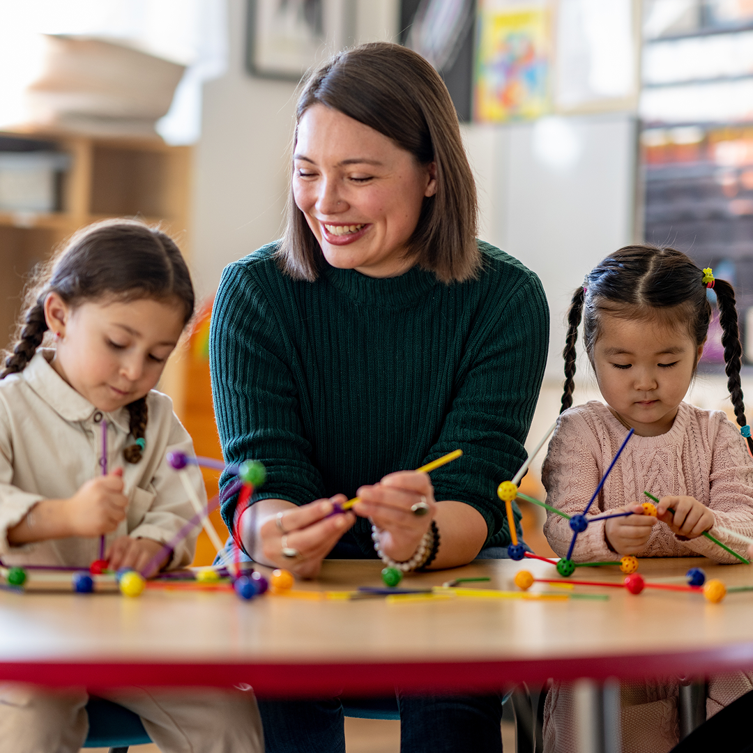 Female educator with two preschool children engaing in a robotics for kids learning session.